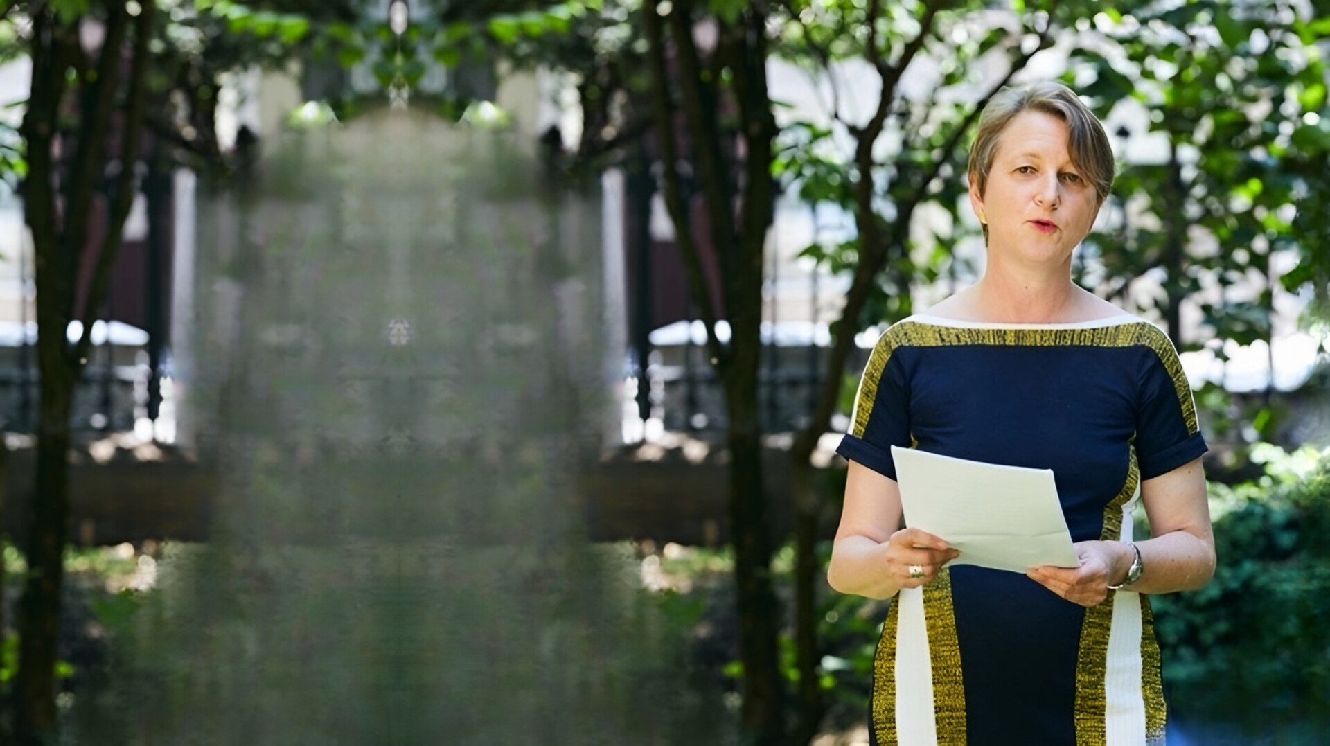 Anja Klug intervient lors d’un événement dans une cour-jardin et s’adresse au public, des notes à la main.